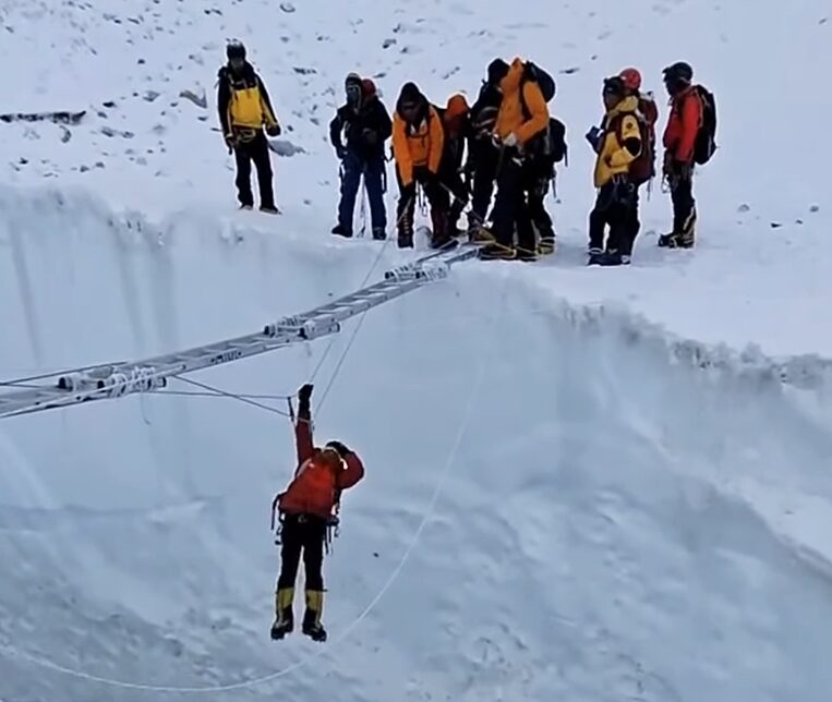 man dangling from ladder over open crevasse