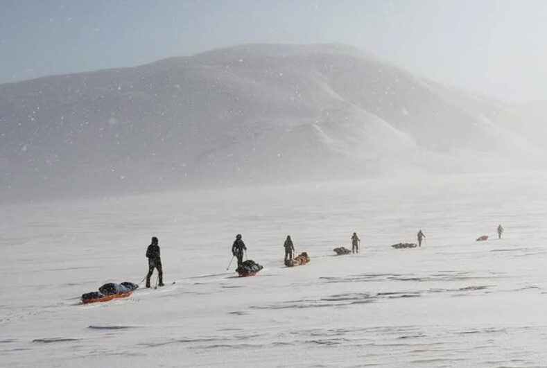 line of skiers pulling sleds in a fog