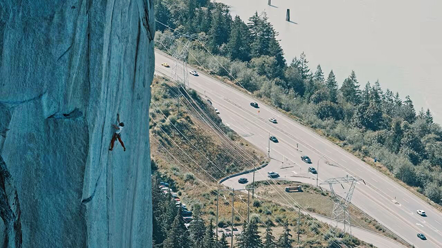 climber on cliff with many cars below