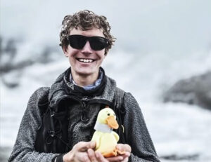 Tyler Andrews holds a stuffed duck and smiles at Everest Base Camp .