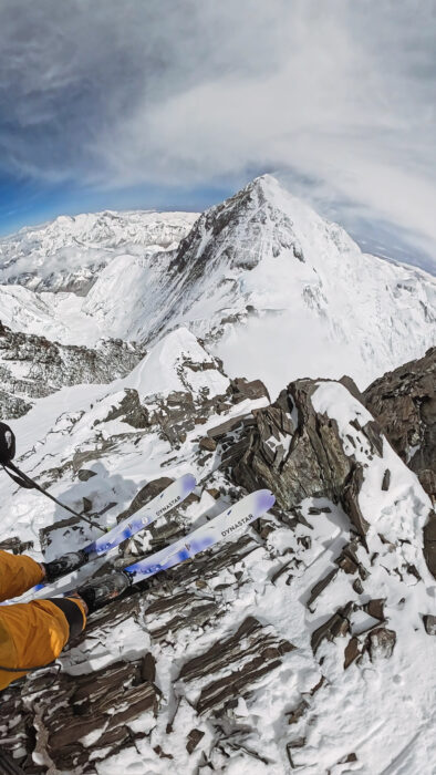 GoPro shot of a pair of skis edging down a rocky section, with Everent in background. 