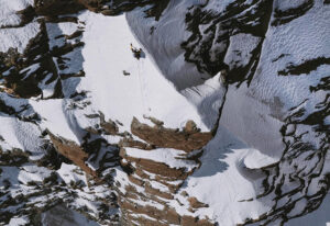 A climber on a snow section of a vertical, mixed face in the Alps.