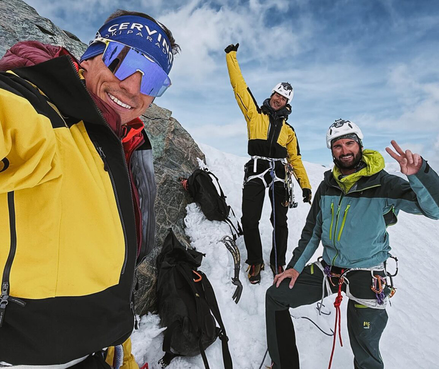 Young climbers smile to the camera on a snowy summit.