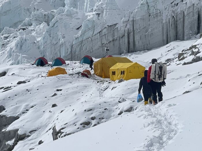 Climbers approaching some tents in front of a vertical serac wall. 