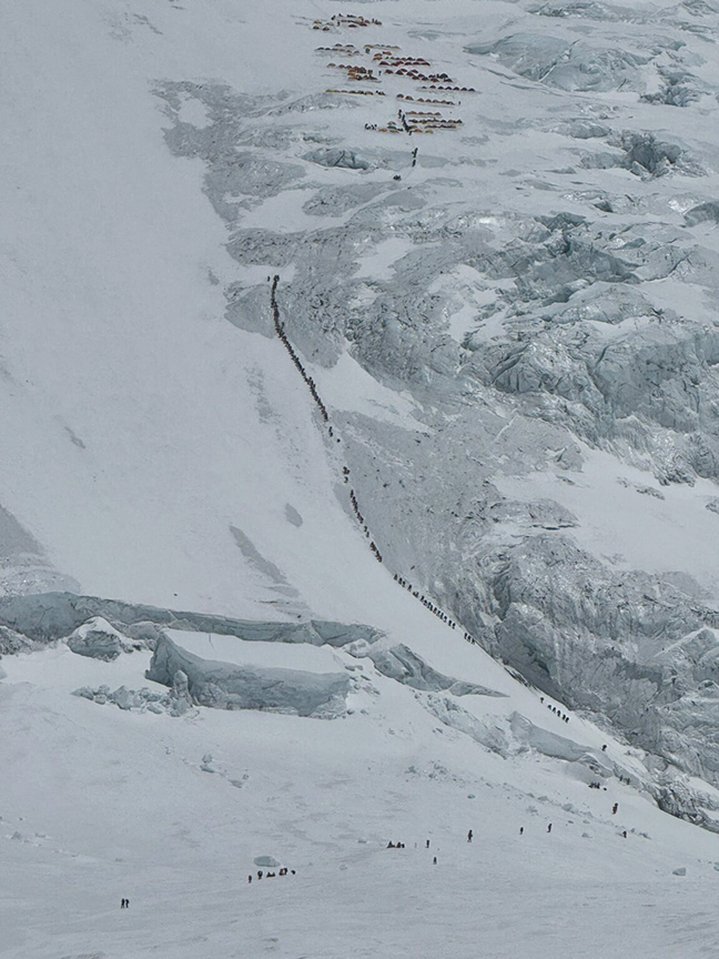 giant line of tiny climbers snaking up mountain