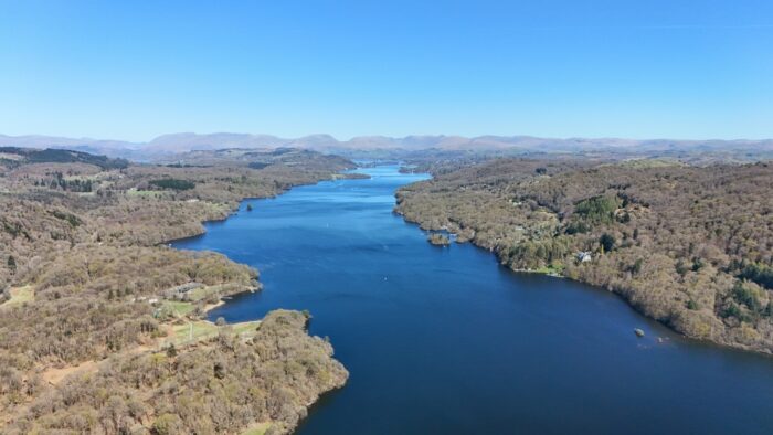 Panoramic aerial view of Windermere lake surrounded by woodland and hills under a clear springtime sky