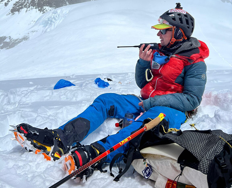 climber sits and speaks into a walkie talkie