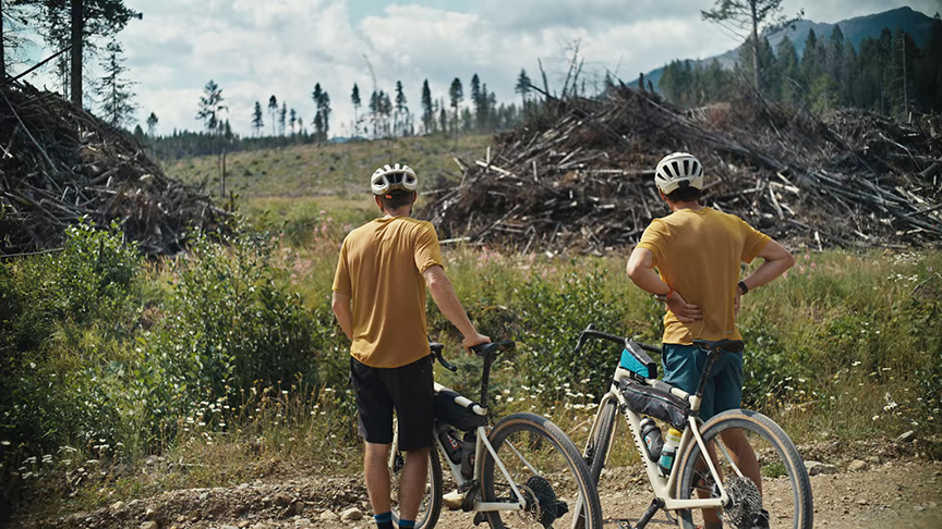 Two men standing with bikes, looking at logging