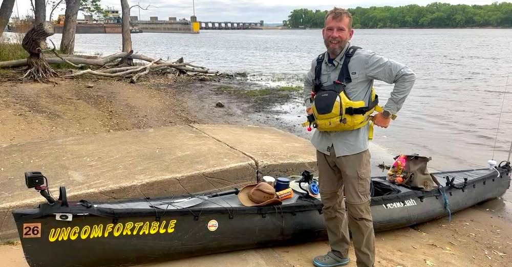 man standing beside kayak on sandy shore