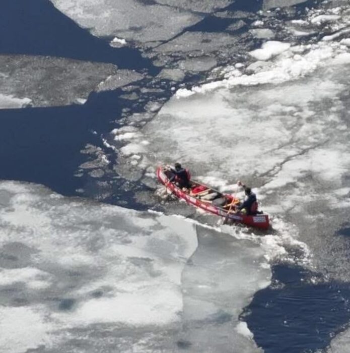 Two canoeists paddling through large pans of thin ice