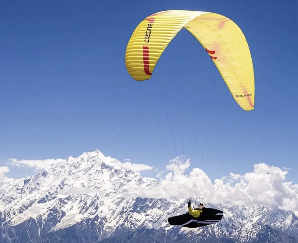 A paraglider with big, snowy Pakistan peaks in background.