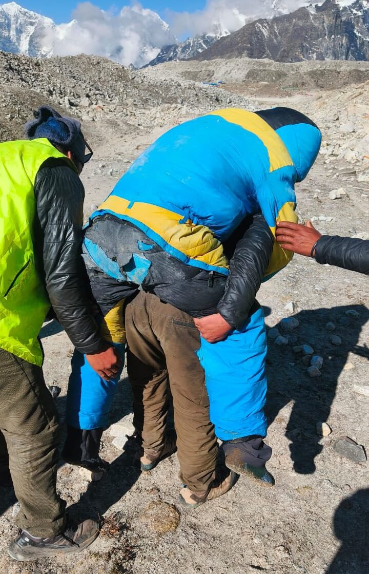 Three people help carry a semi-unconcious Sherpa with ragged high-altitude clothes.