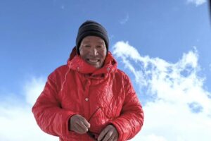 Close shot of a Sherpa climber with a wooden cap and a red jacket.