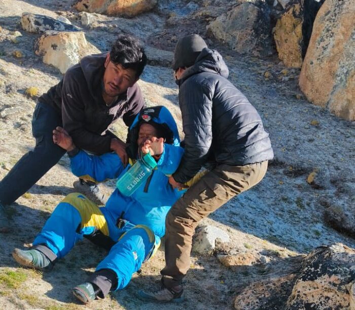 Two workers help an exhausted sherpa laying on the rocky ground. 