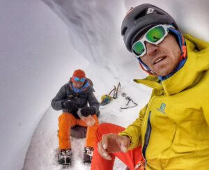 Two climbers sitting on an ice ledge under a serac.