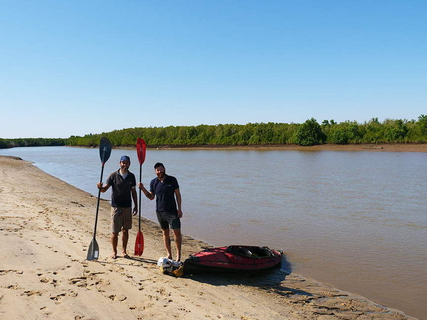 Two men standing beside a river holding paddles