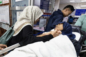woman in kerchief lying on hospital cot embraced by family