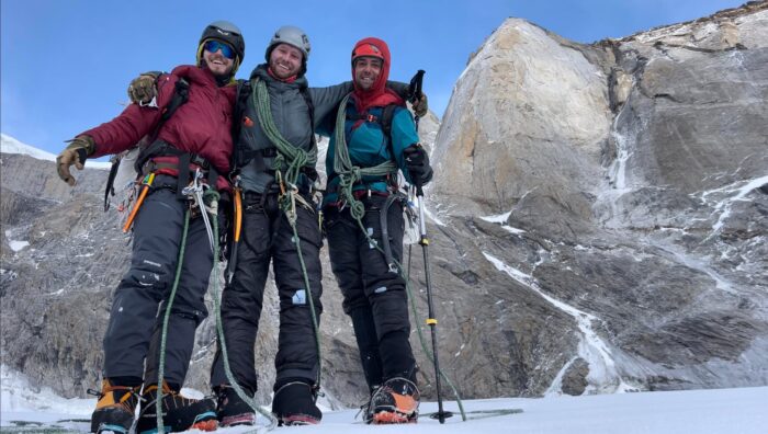 Three climbers pose in front of a vertical rock face. 