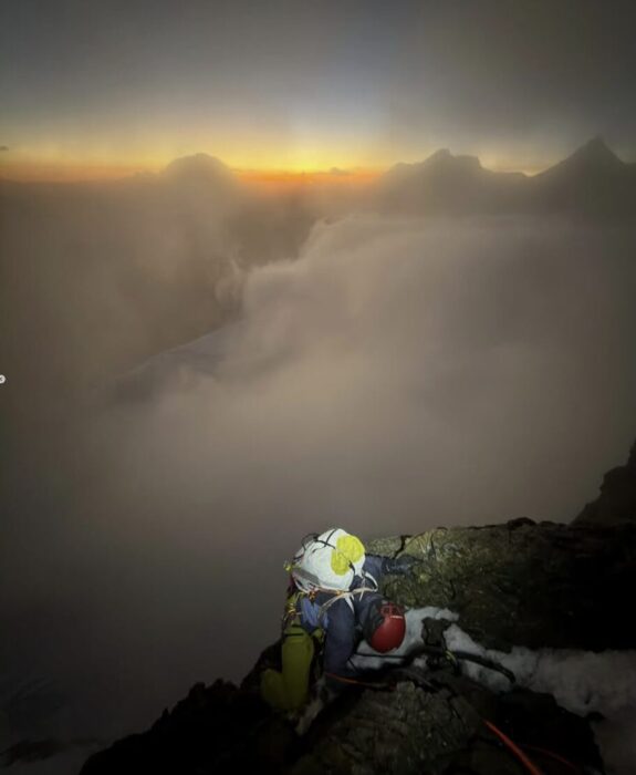 A climber on a rocky spur, right below the line of clouds at sunset.