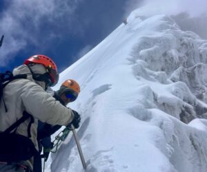 Climbers on a steep snow slope holding ice axes.