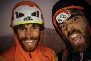 Close shots of two climbers in an indoor setting but with helmets and headlamps still on.