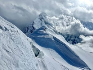 A climber on a snowy ridge surrounded by clouds.