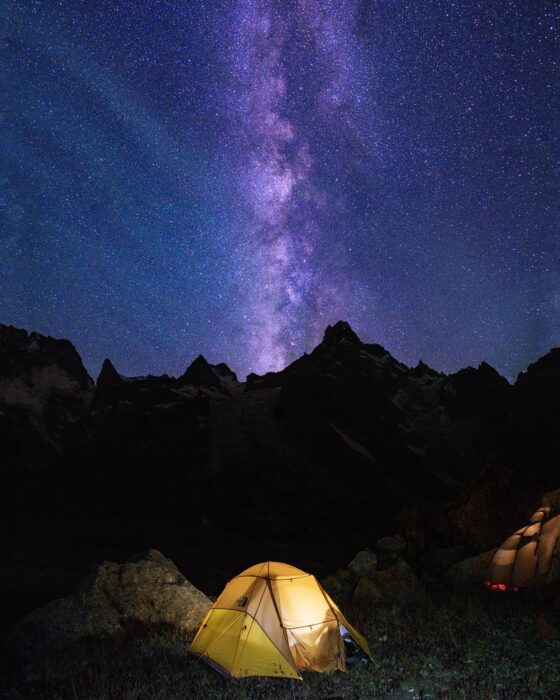 A tent lit up in the night, the Milky Way above.