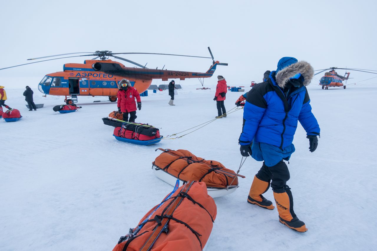 Skiers with sleds and orange helicopter in background
