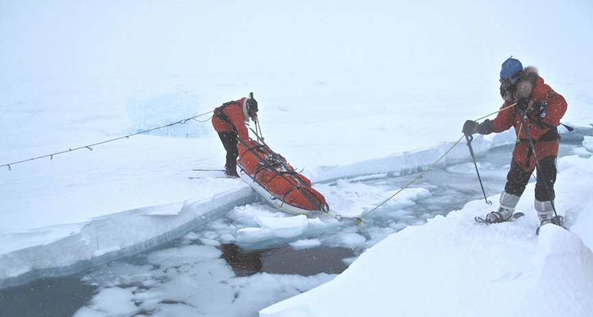 skiers maneuver sled over crack in ice