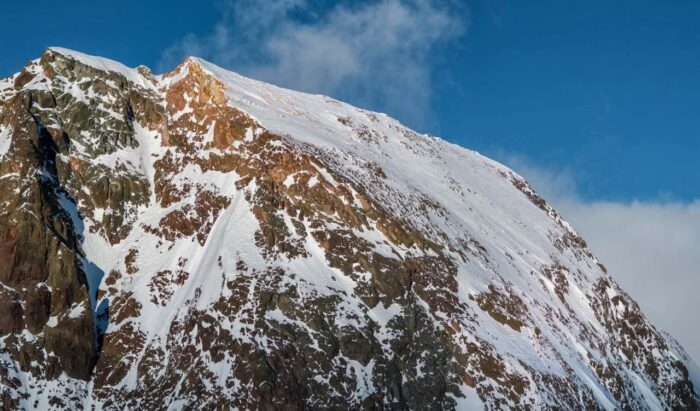 A line of climbers on a huge snow and rock face. 