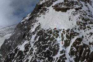Two climbers belay another one on a big mixed face.