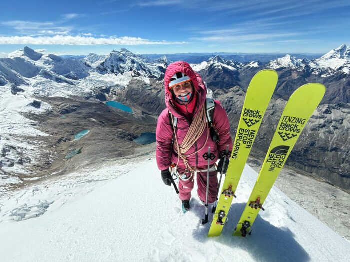 Fay manners on a snowy summit with her skis stuck in the snow by her side.