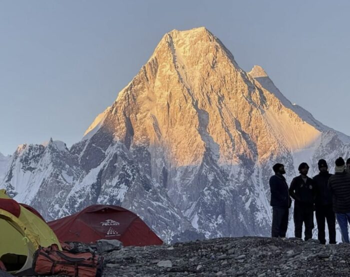 Climbers contemplate Gasherbrum IV's Shining Wall by their tents.