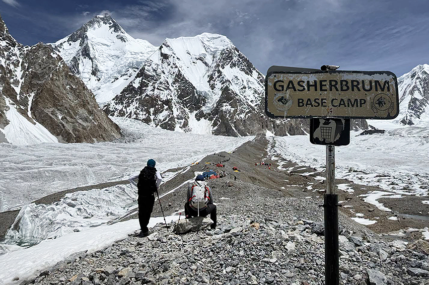 Two climbers look ahead at a flat morraine by a signal marking Gasherbrum Base Camp.