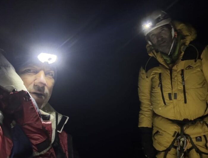 Two climbers in the night, their faces lit up by headlamps.