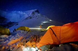 Climbers' headlamps march toward a summit in the night, from a group of tents.