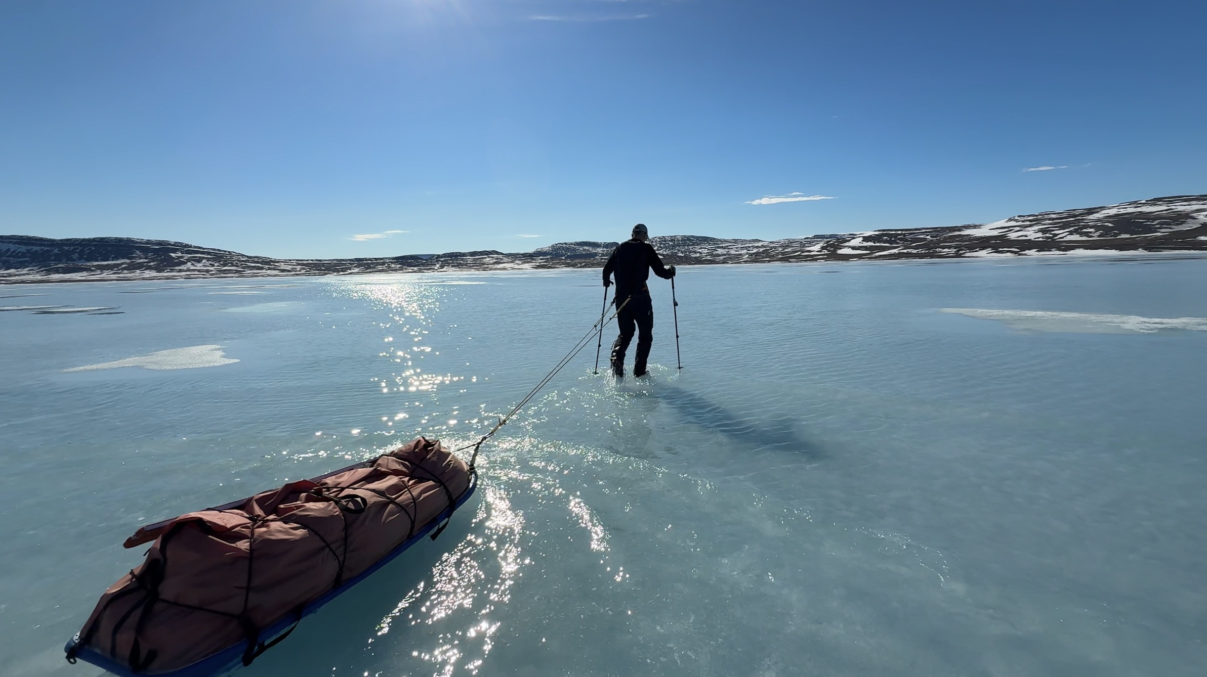 sledder hauls through meltwater atop sea ice
