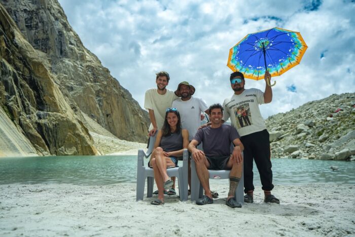 Climbers sitting by a river, a Pakistani assistant holding an umbrella.