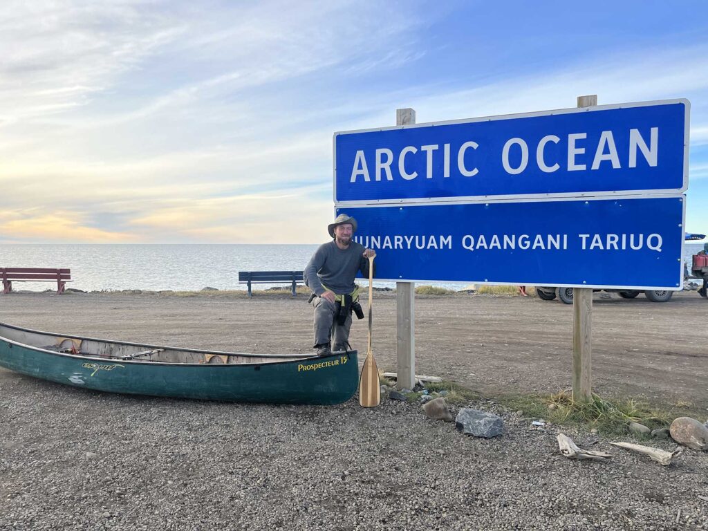 guy standing beside his canoe at Arctic Ocean sign