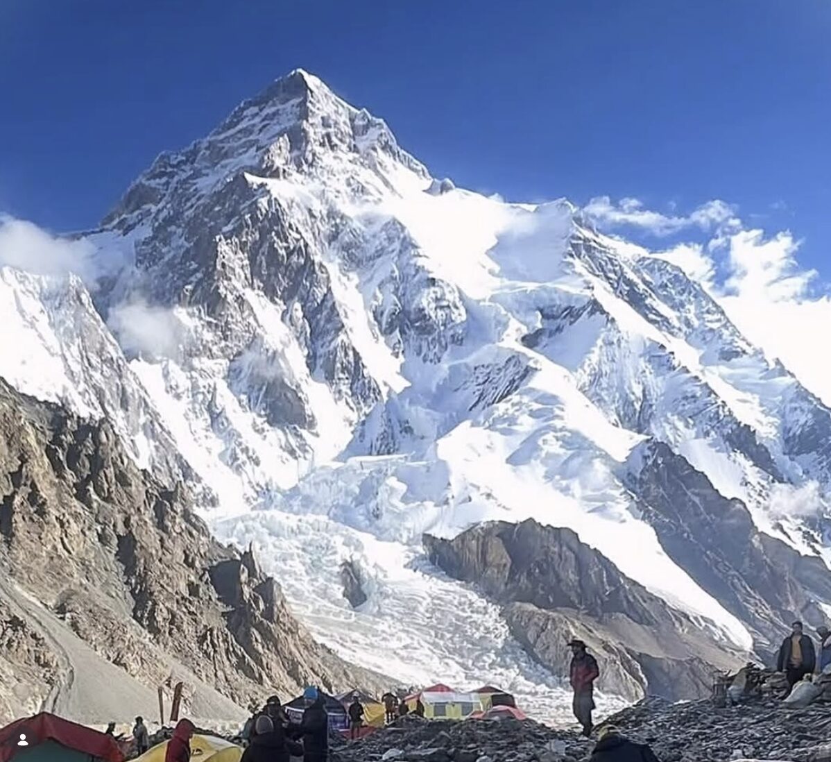 K2 on a bright day with a porter in Base Camp in front of the mountain.