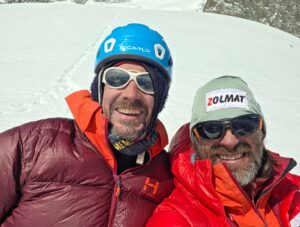 Two climbers with a snow background, with helmets, sunglasses and dawn jackets.