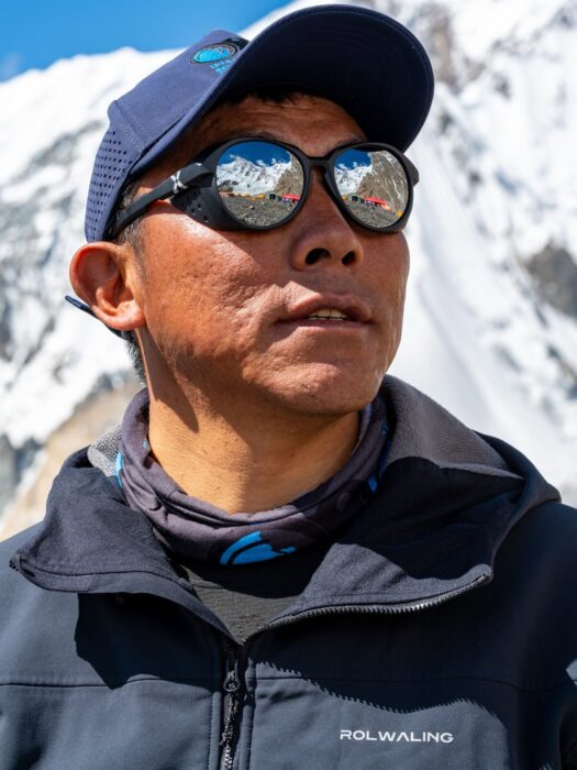 Close shot of Mingma G with a cap and round, mirrowed sunglasses. 