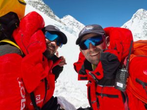 Close shots of two Pakistani climbers in bright red dawnsuits, sunglases and caps.
