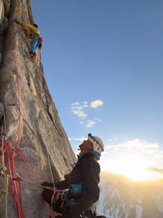 A climber belays his partner on a granite wall at sunset. 