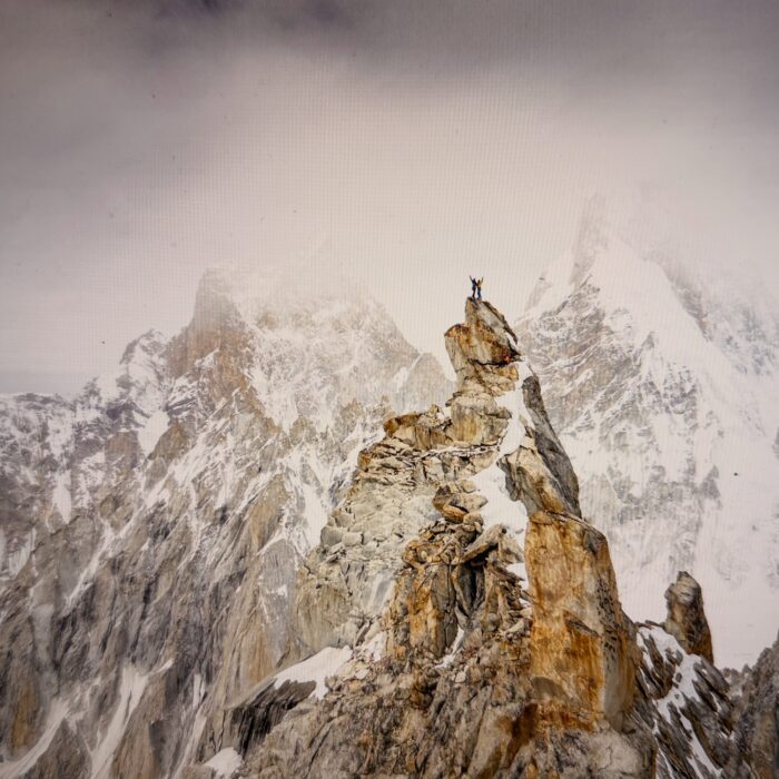 A rocky spire with three people on the tiny top. 