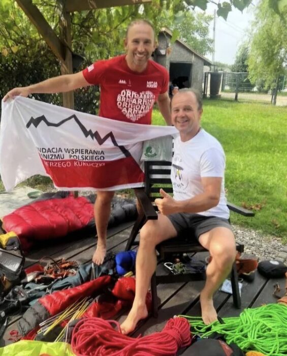 Two climbers in shorts and tshirts hold an expedition banner in a hotel's garden.
