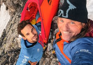 To climbers take a selfie by their tiny tent at a rocky bivy site.