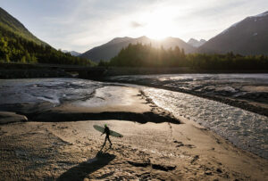 A surfer walks across the mud flats to try and catch the tidal bore wave at Turnagain Arm.