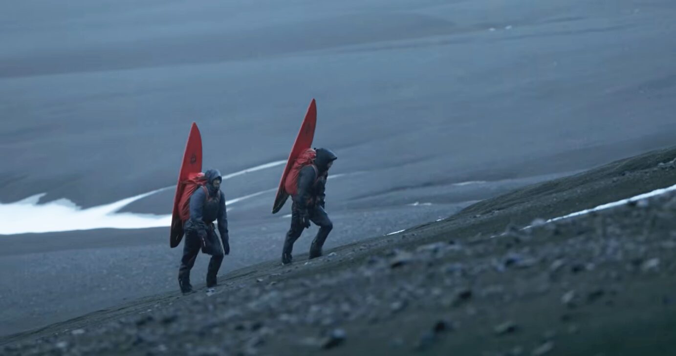 Two men with surfboards walk up a slate hill