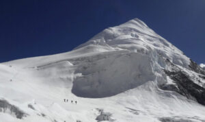 Climbers on a snowy peak, walking to the left to avoid a gib serac barrier towards a col.